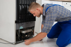Technician repairing refrigerator in home.