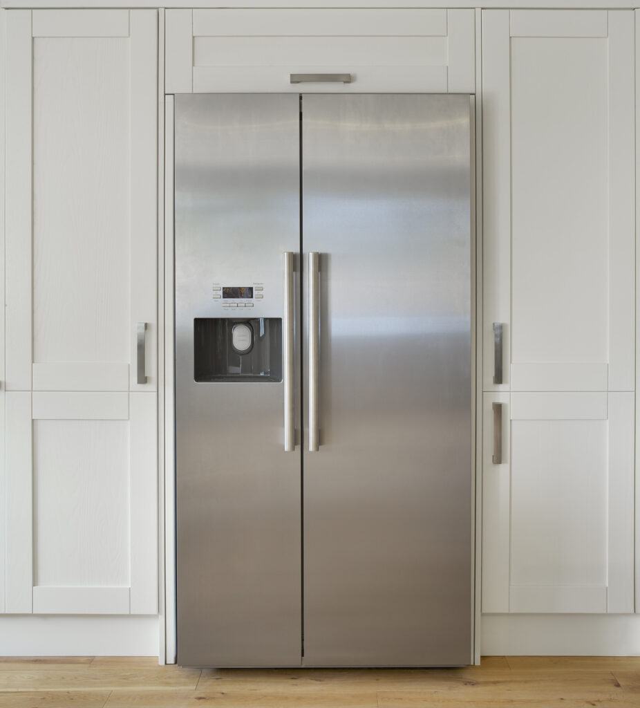 a modern American fridge freezer set into a bank of cream coloured cupboards in a farmhouse-style kitchen. Made from brushed stainless steel.
